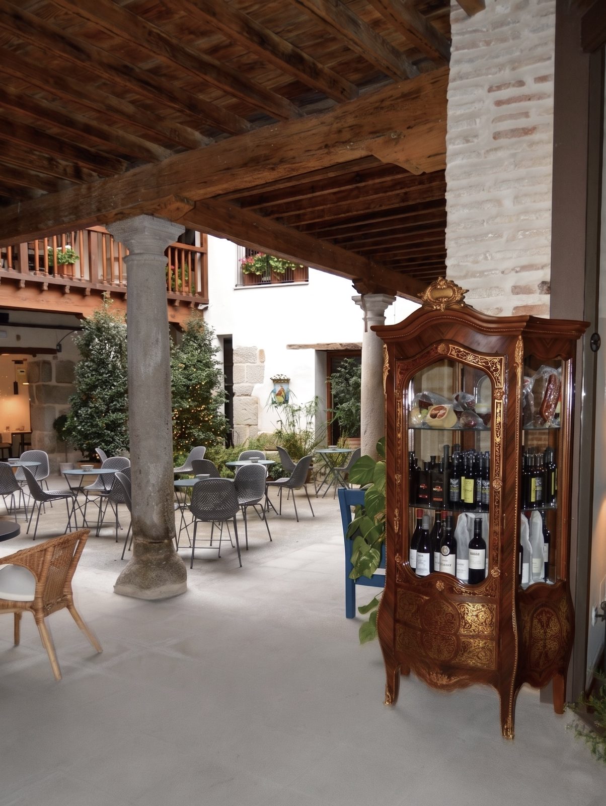 Patio del Casón del Conde bajo el techo de vigas, con columna de piedra, mesas y una vitrina de vinos