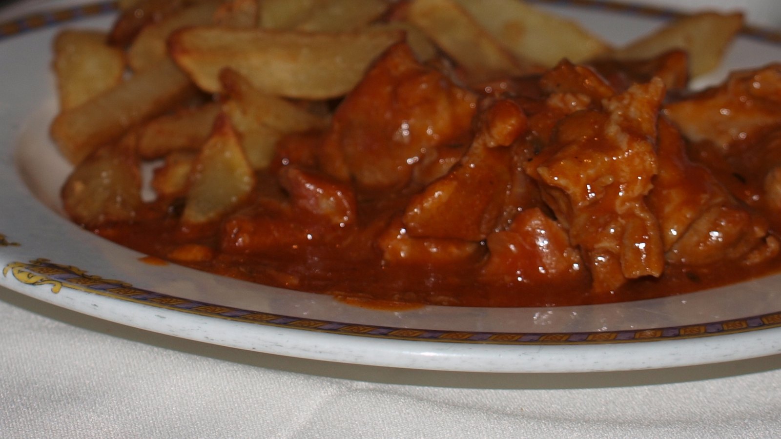 Plato de carcamusas toledanas, guiso de cerdo con tomate, servido con patatas fritas