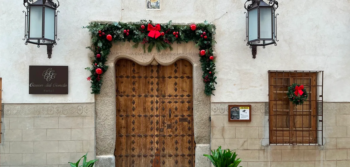 Portón de madera del Casón del Conde en Orgaz con una guirnalda de Navidad y el cartel del hotel