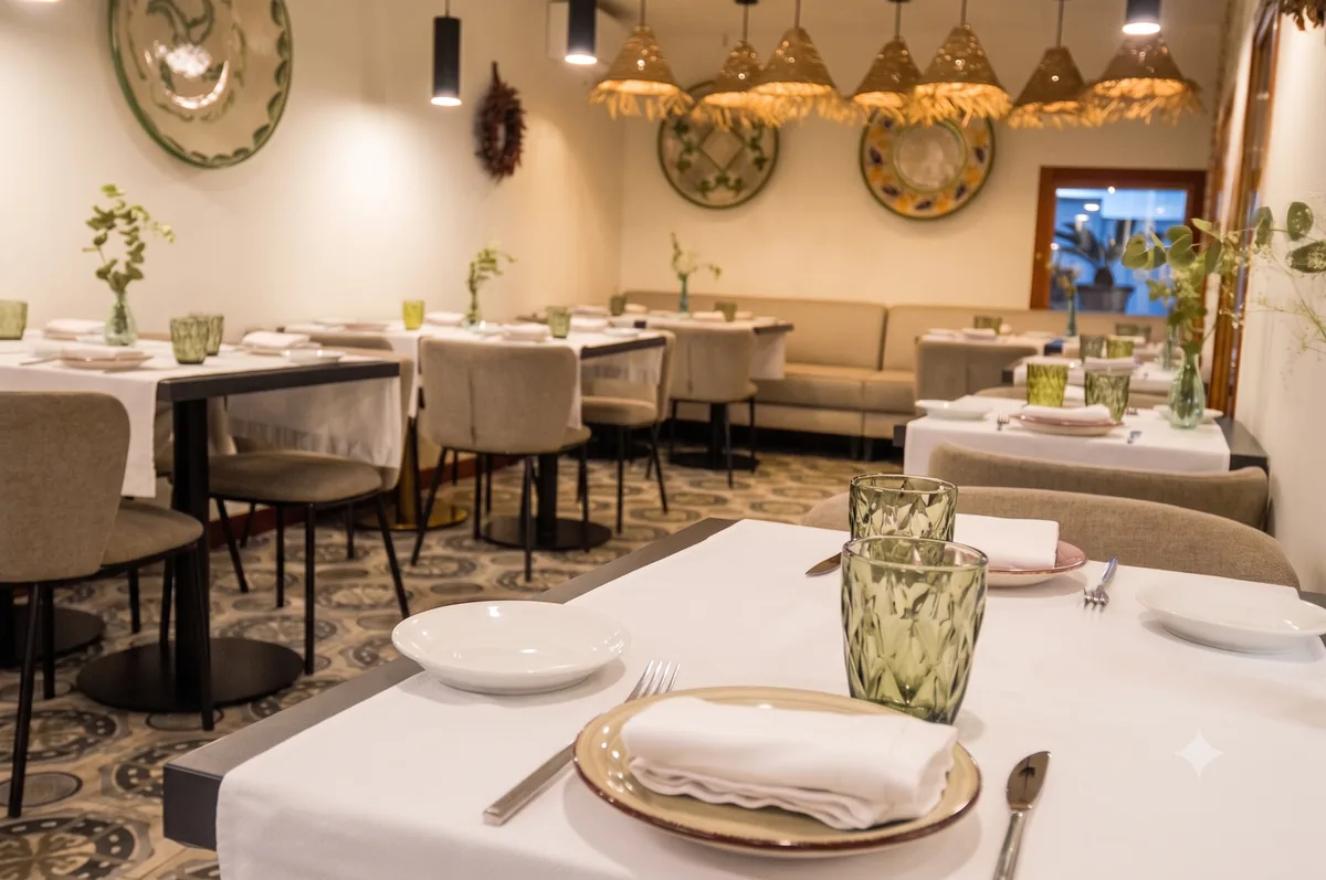 Mesa puesta en el comedor de La Condesa, con mantel blanco, platos de borde dorado y copas verdes labradas