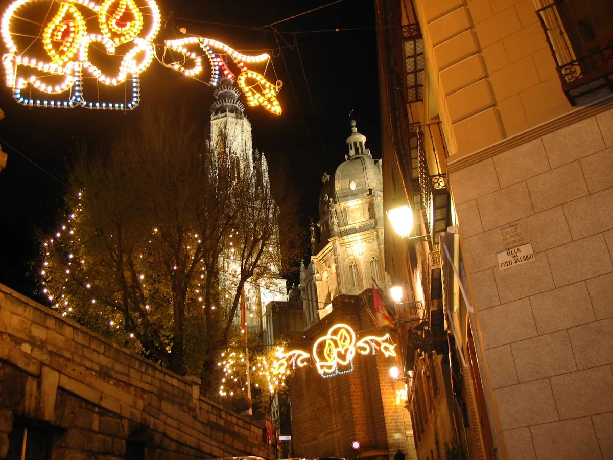 La Catedral de Toledo de noche, con la torre y la cúpula iluminadas y adornos de luces de Navidad en la calle