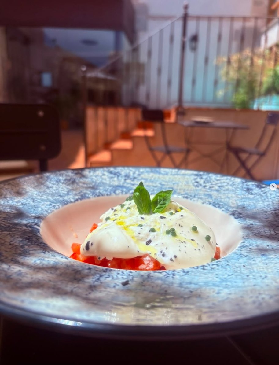 Burrata sobre tomate con albahaca y aceite, con la terraza al fondo