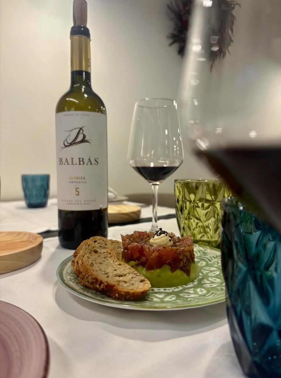 Tartar de atún sobre crema de aguacate, con pan de semillas y una copa de vino en la mesa de La Condesa