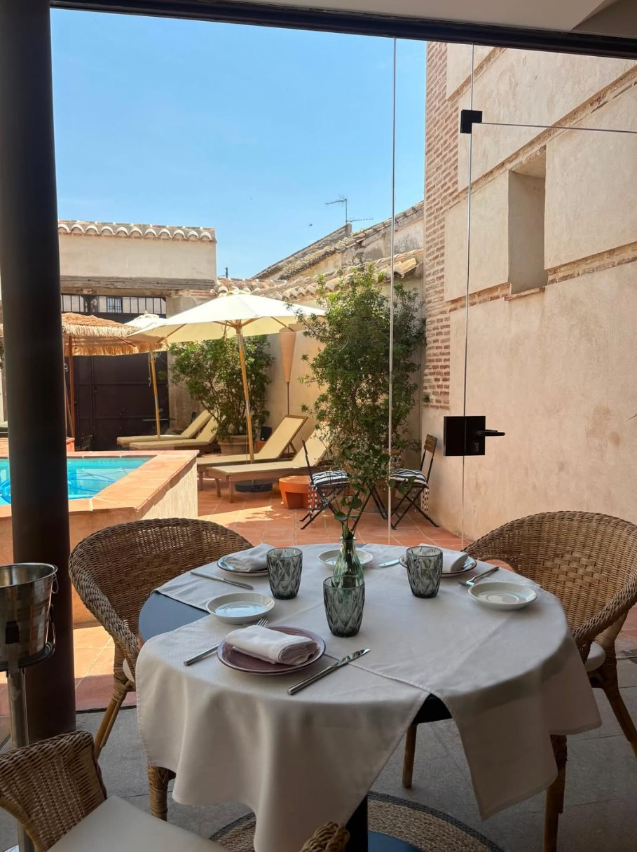 Mesa puesta en la terraza de La Condesa con la piscina y las tumbonas al fondo