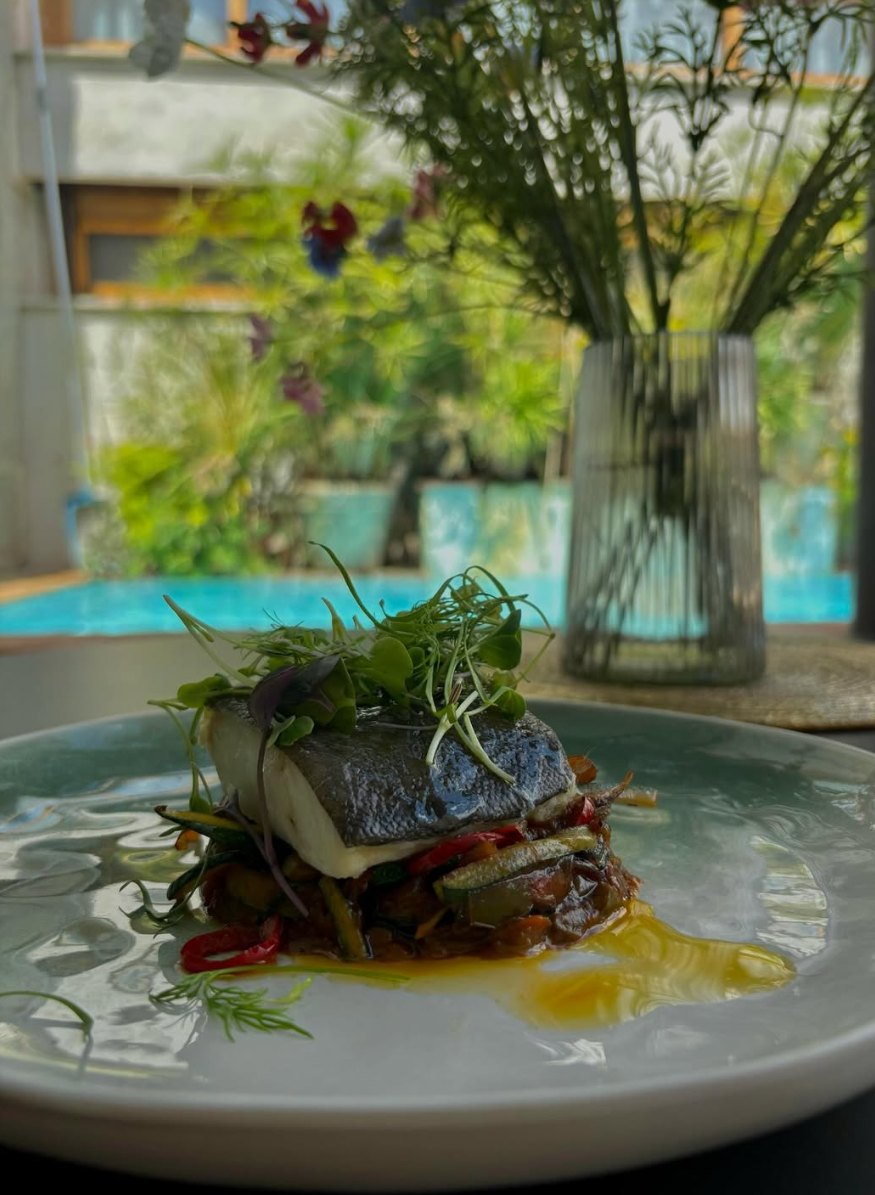 Lomo de pescado sobre pisto de verduras, con la piscina del patio del Casón del Conde al fondo